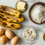 The Best Moist & Easy Gluten Free Banana Bread 7 Ingredients for gluten-free banana bread, including ripe bananas, GF flour, and eggs, arranged on a white marble surface.