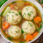 Amazing Vegan Matzo Ball Soup (The Secret to No-Crumble Balls) 7 Hero image of vegan matzo ball soup in a rustic bowl with golden broth, fluffy matzo balls, fresh dill, carrots, and celery